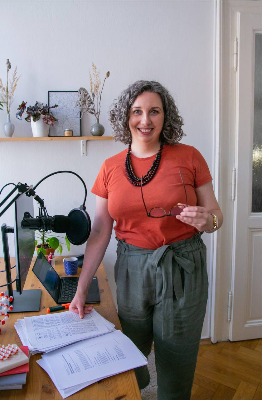 Dr Anna Clemens standing next to her desk, holding her glasses in her hand