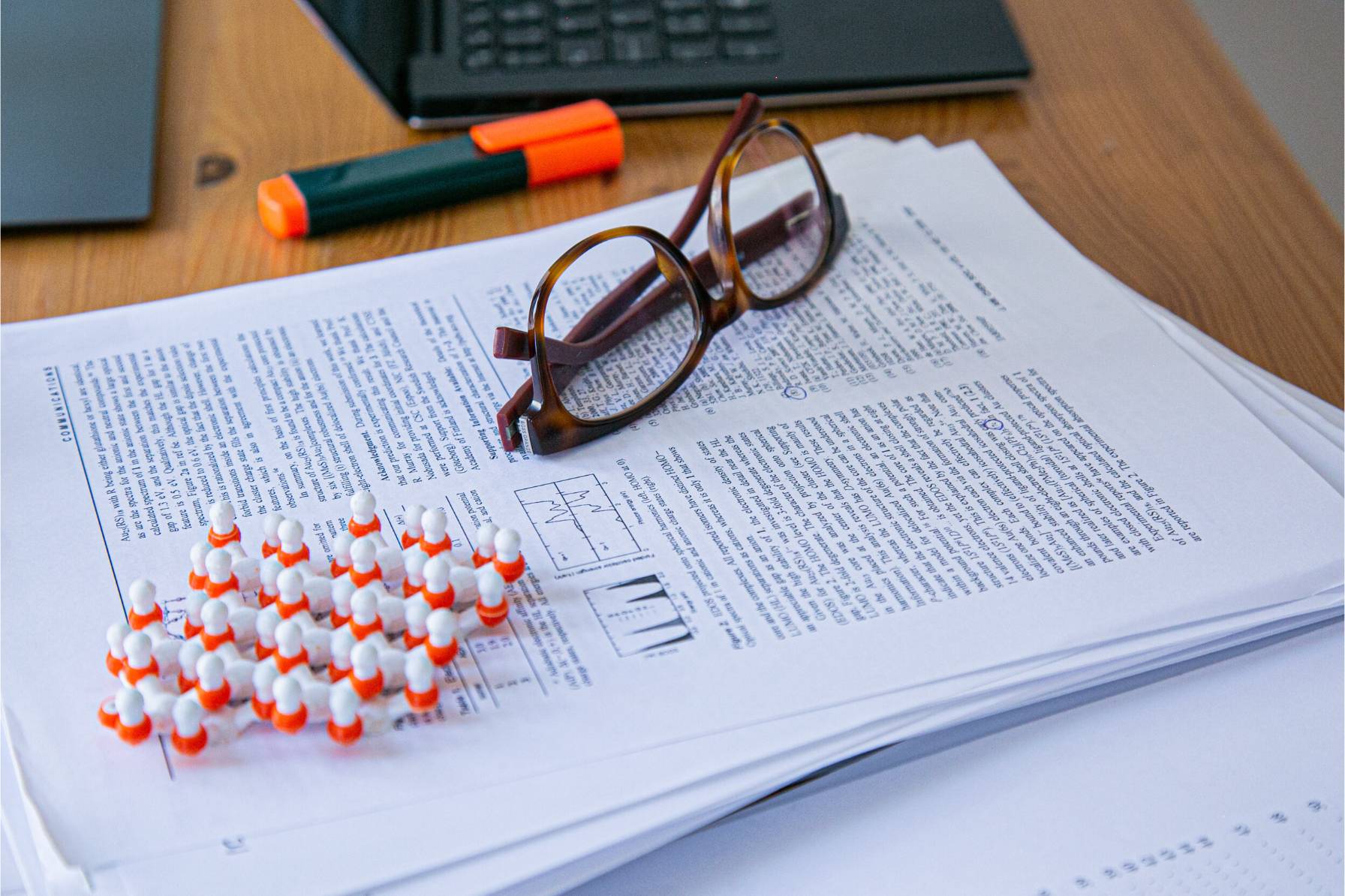 Stack of academic papers and Anna's glasses on her desk