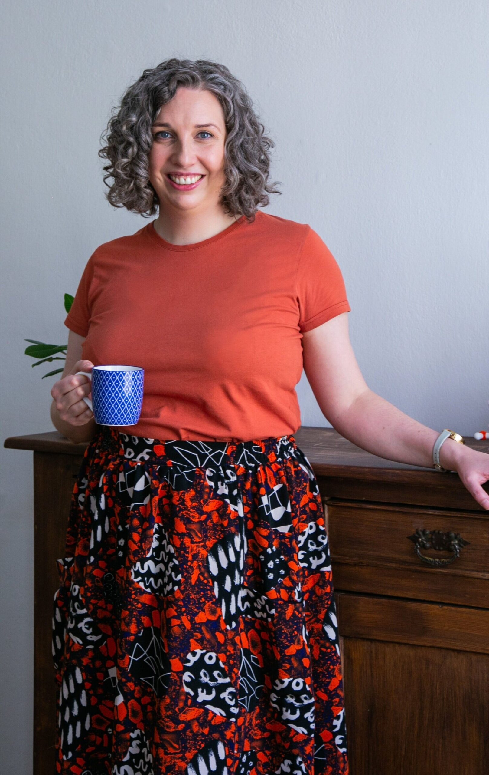 Dr Anna Clemens standing with her arm resting on a credenza, holding a mug.