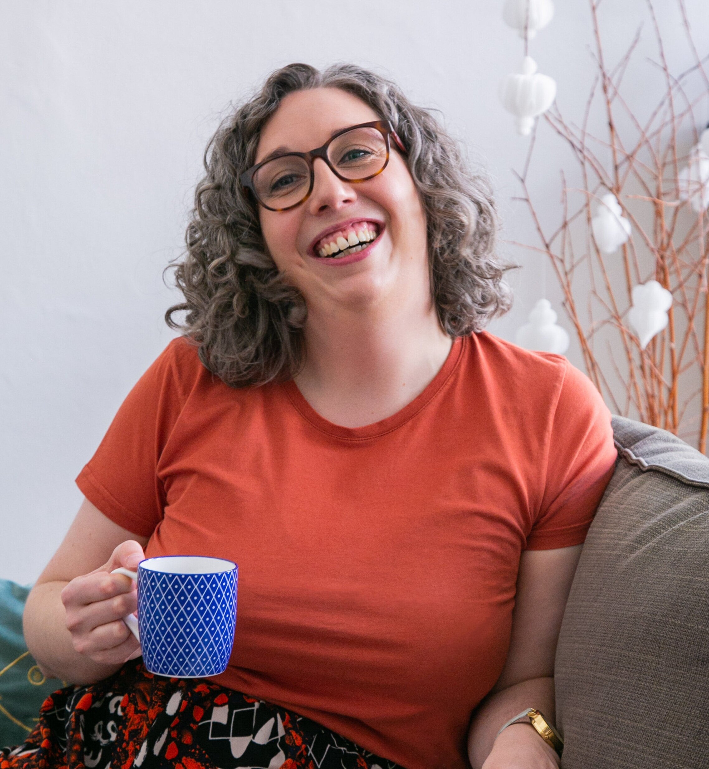 Dr Anna Clemens laughing on a couch, holding a mug.