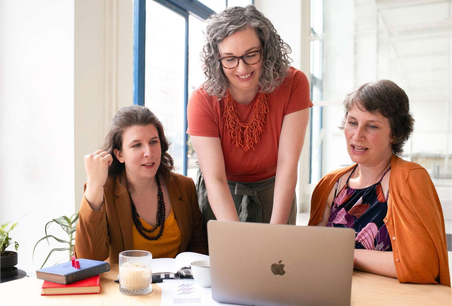 Dr Anna Clemens smiling while working at a laptop in between the Researchers' Writing Academy assistants Andrea Frye and Yvonne Rimar