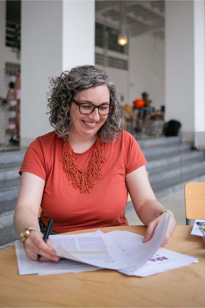 Dr Anna Clemens, founder of the Researchers' Writing Academy, sits at a desk, smiling while reviewing sections of an academic paper.