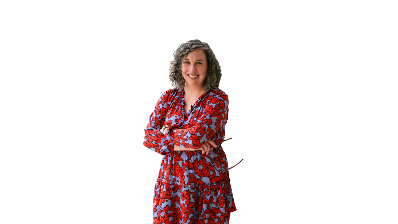 A person with curly hair smiles while standing with their arms crossed. They are wearing a red and blue patterned dress. The background is transparent.